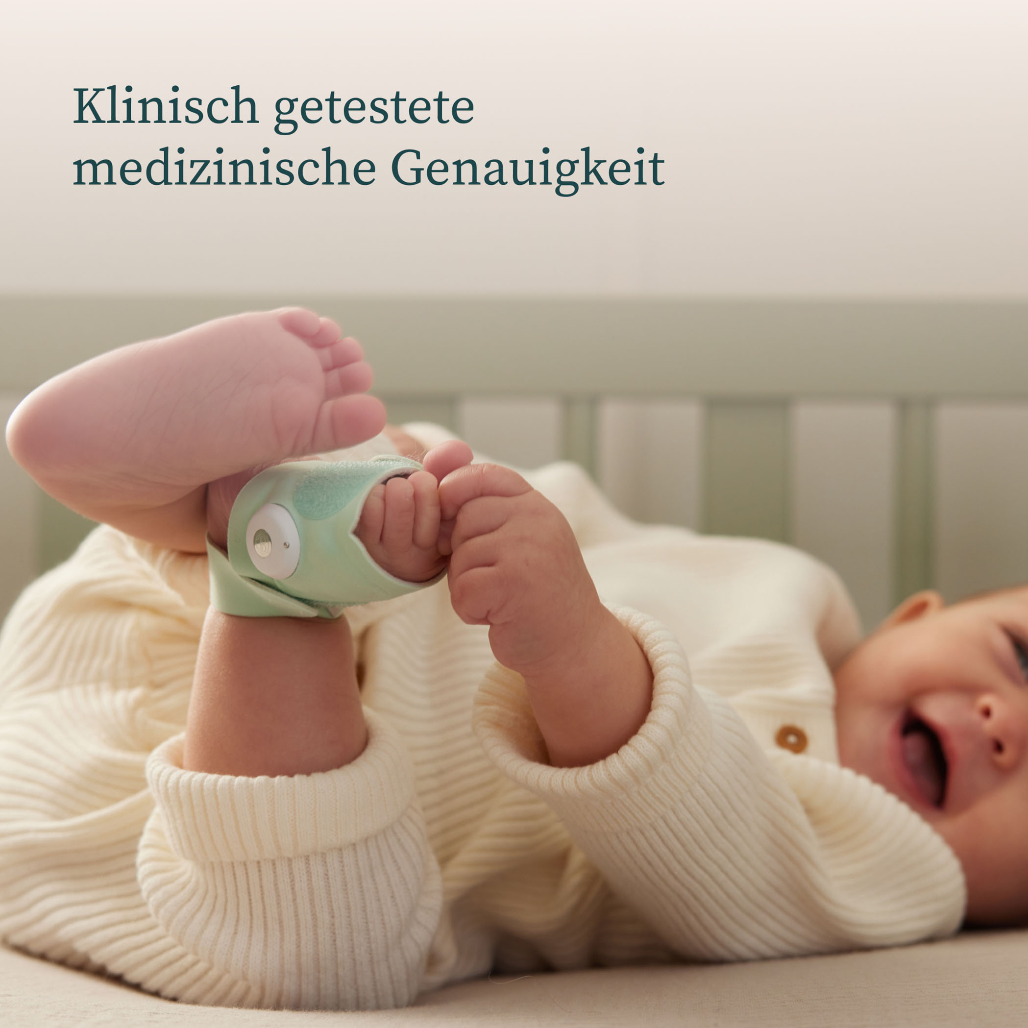 Baby im Bett, trägt grünes Gerät am Fuß. Text auf Deutsch darüber.