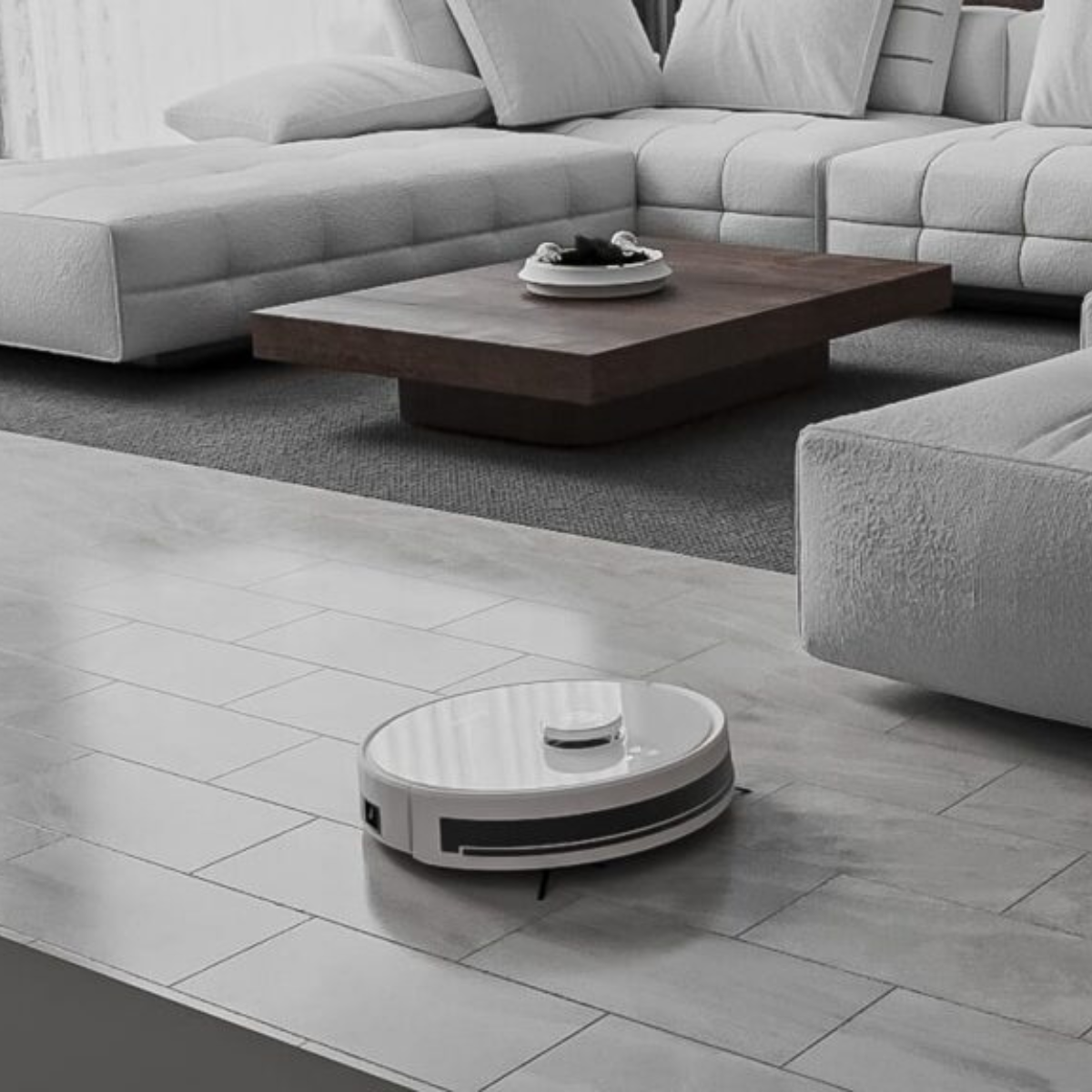 Roboter-Staubsauger auf Fliesenboden. Hellgraue Fliesen, weißes Sofa und brauner Couchtisch.