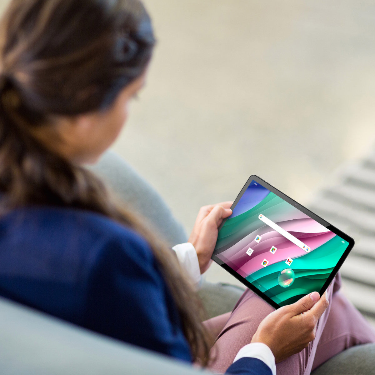 Donna seduta, tiene in mano un tablet con schermo colorato, sfondo sfocato.
