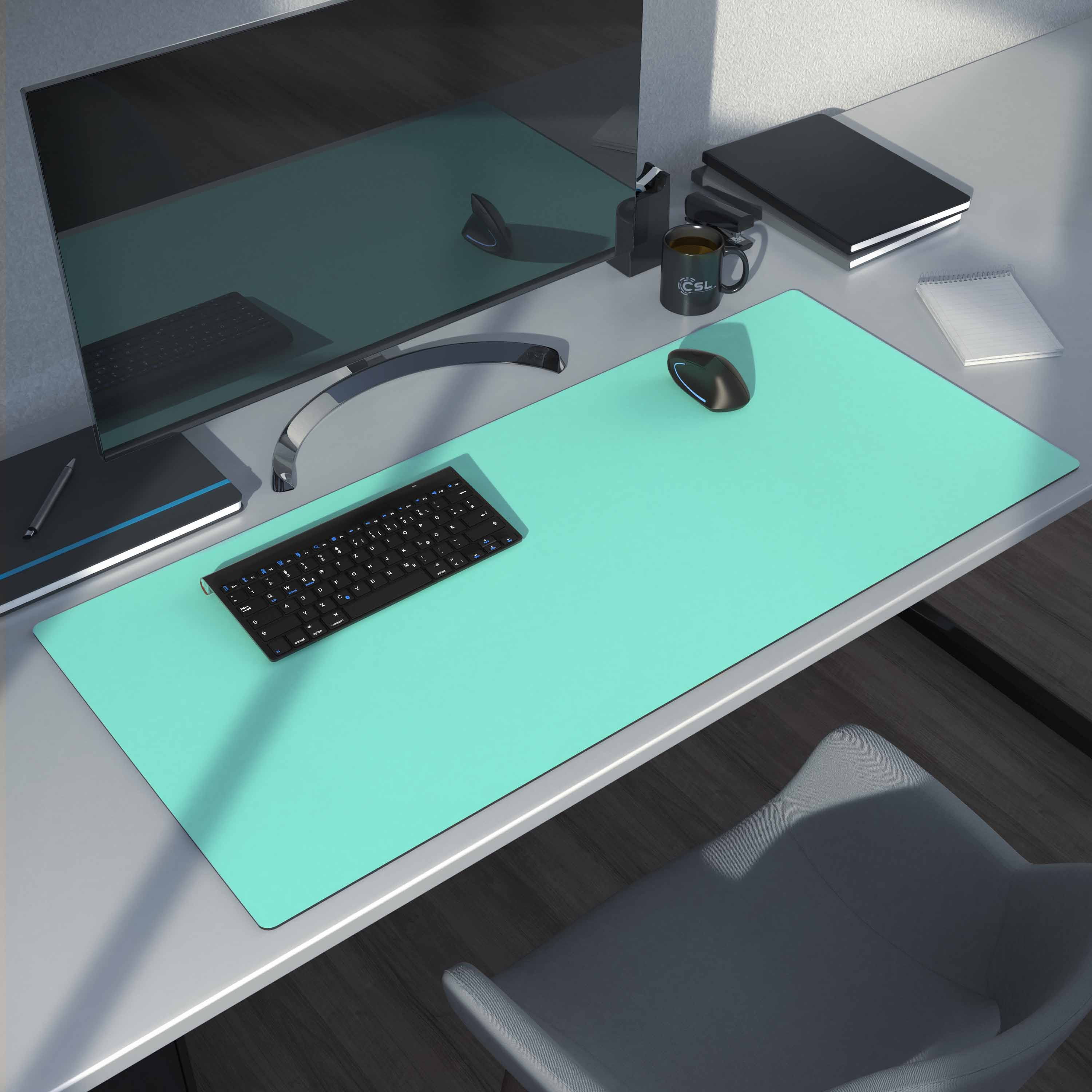 Schreibtisch-Setup mit türkisfarbenem Mousepad, Tastatur, Monitor, Kaffeetasse, Maus und Notizbuch.
