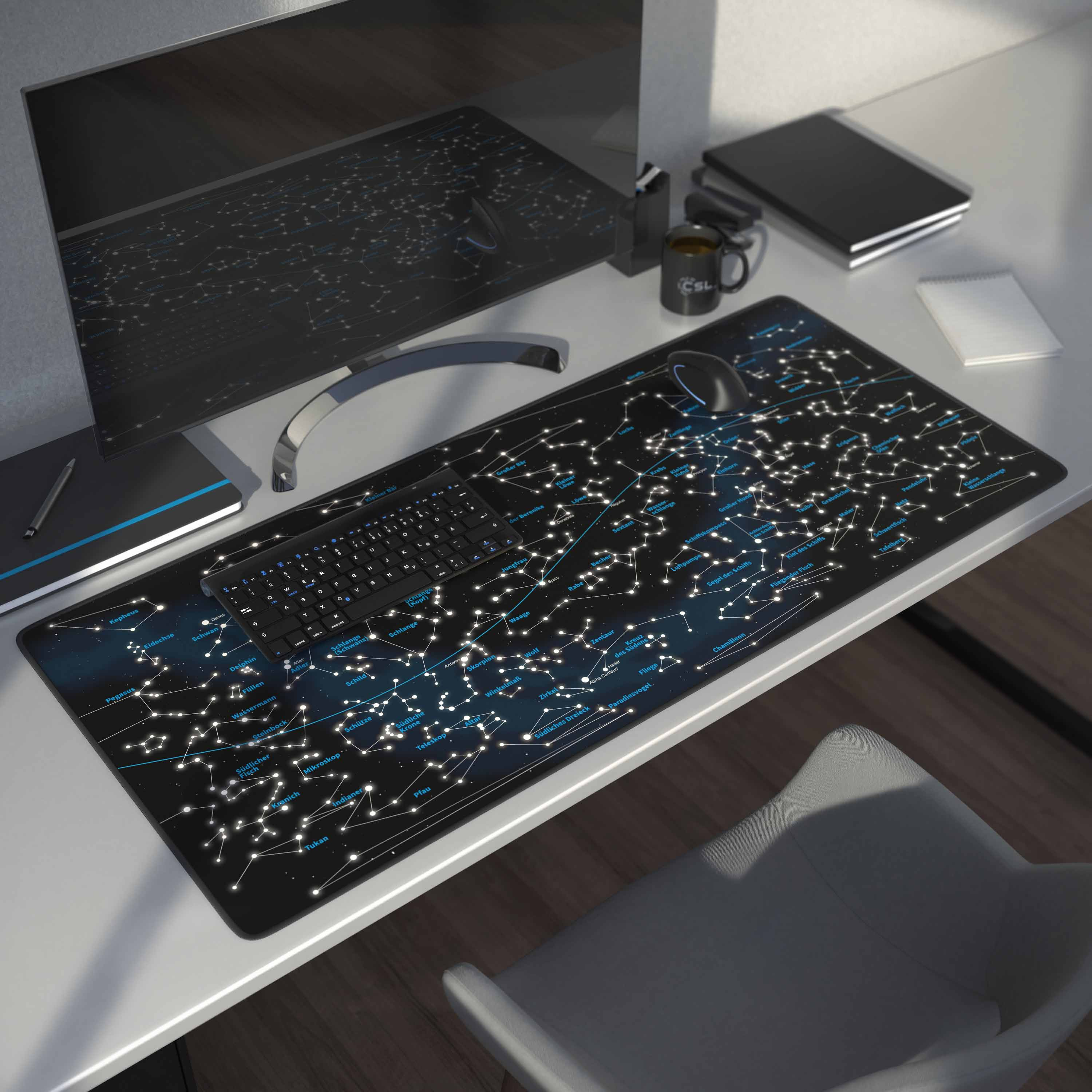 Schreibtisch mit einem Sternbild-Mauspad. Tastatur, Monitor, Tasse und Notizbuch sind ebenfalls sichtbar.