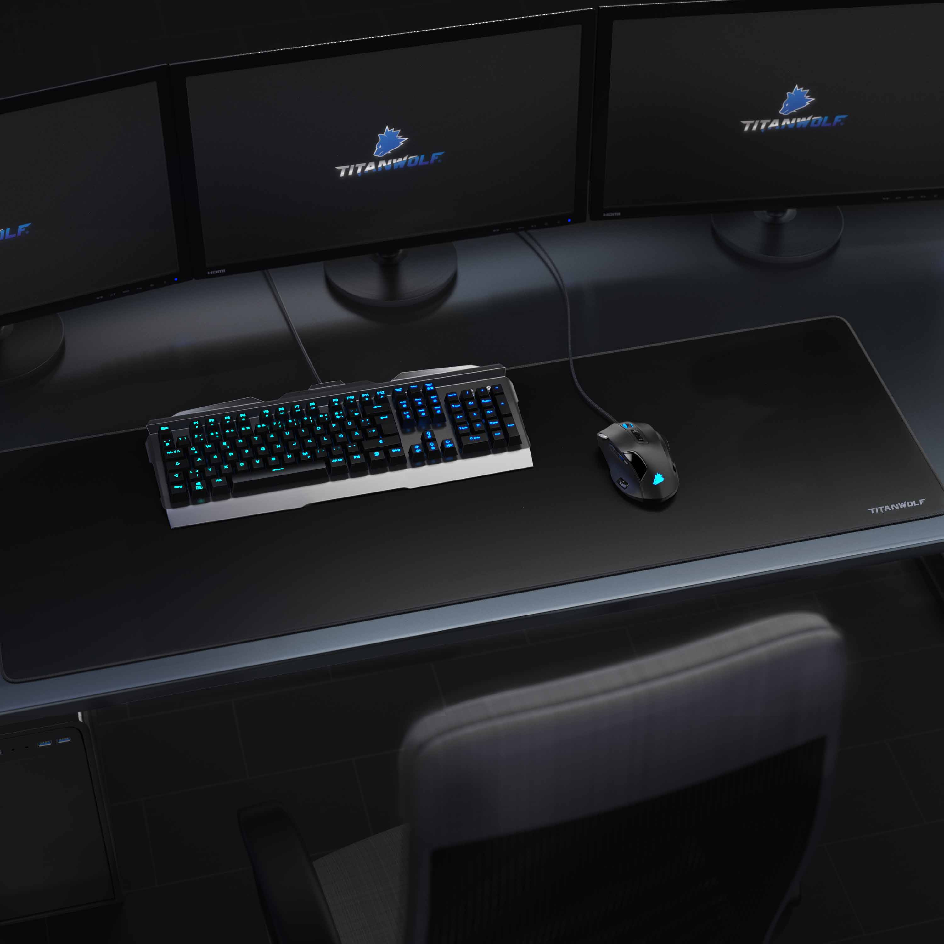 Schreibtisch-Setup mit drei Monitoren, Tastatur, Maus und Mauspad. Ein Stuhl ist sichtbar.