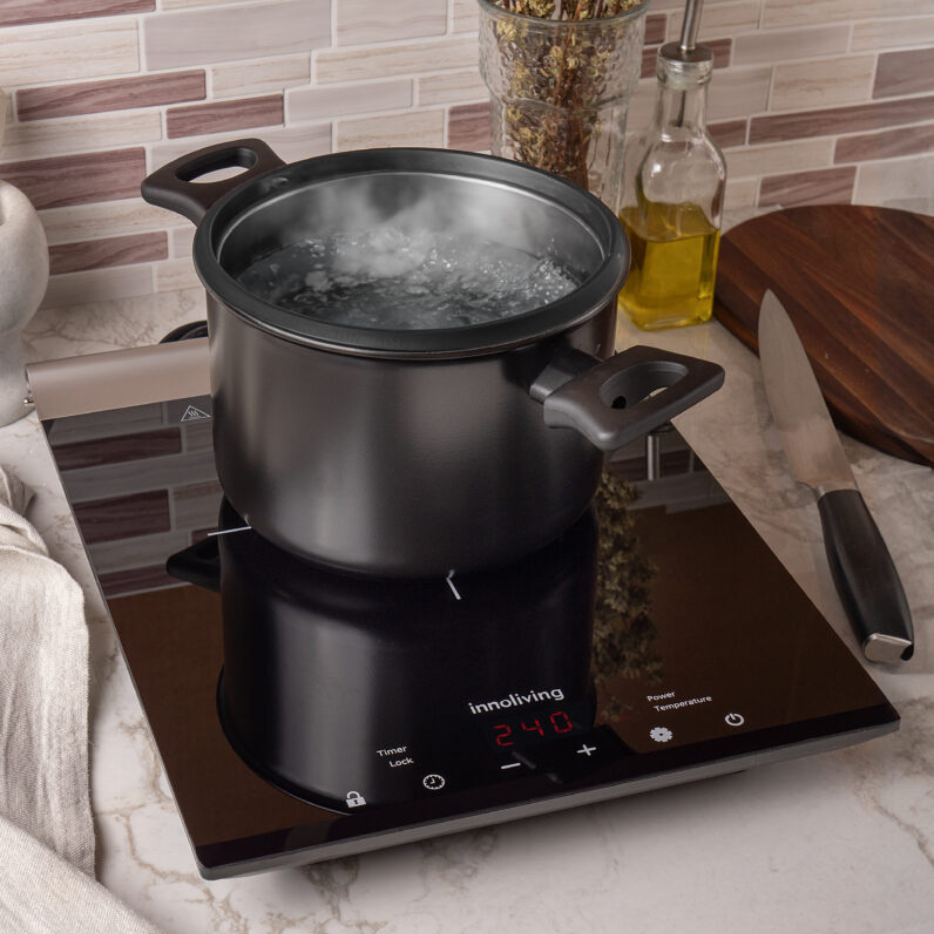Un piano cottura a induzione nero con una pentola di acqua bollente sopra. Il timer mostra 2:40. Coltelli e bottiglia d'olio nelle vicinanze.