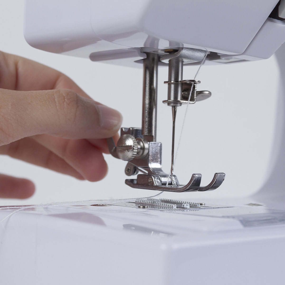 Zbliżenie igły, nici i stopki maszyny do szycia, z dłonią w pobliżu.