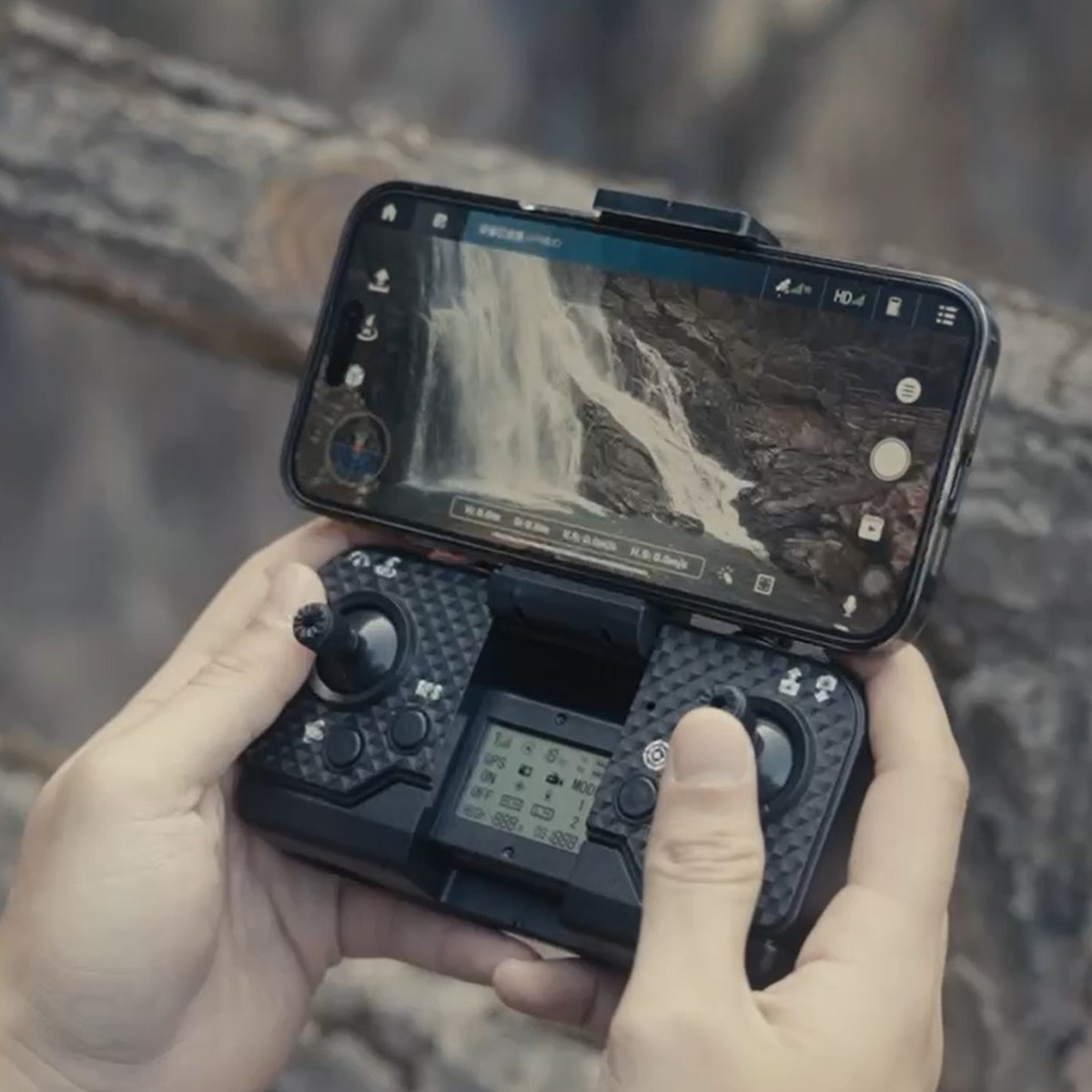 Ręce trzymające czarny kontroler drona z telefonem wyświetlającym wodospad.