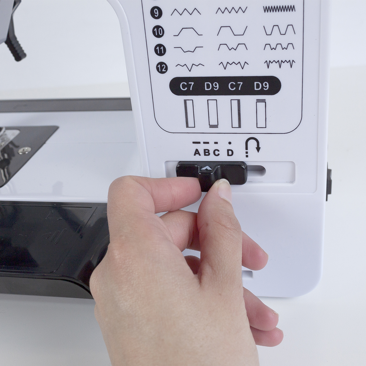 Ręka regulująca pokrętło maszyny do szycia. Biała maszyna, czarne pokrętło.