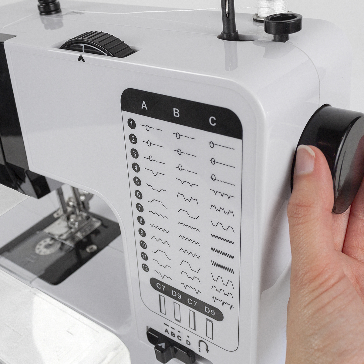 Maszyna do szycia, zbliżenie na panel sterowania. Biała maszyna, ręka na pokrętle.