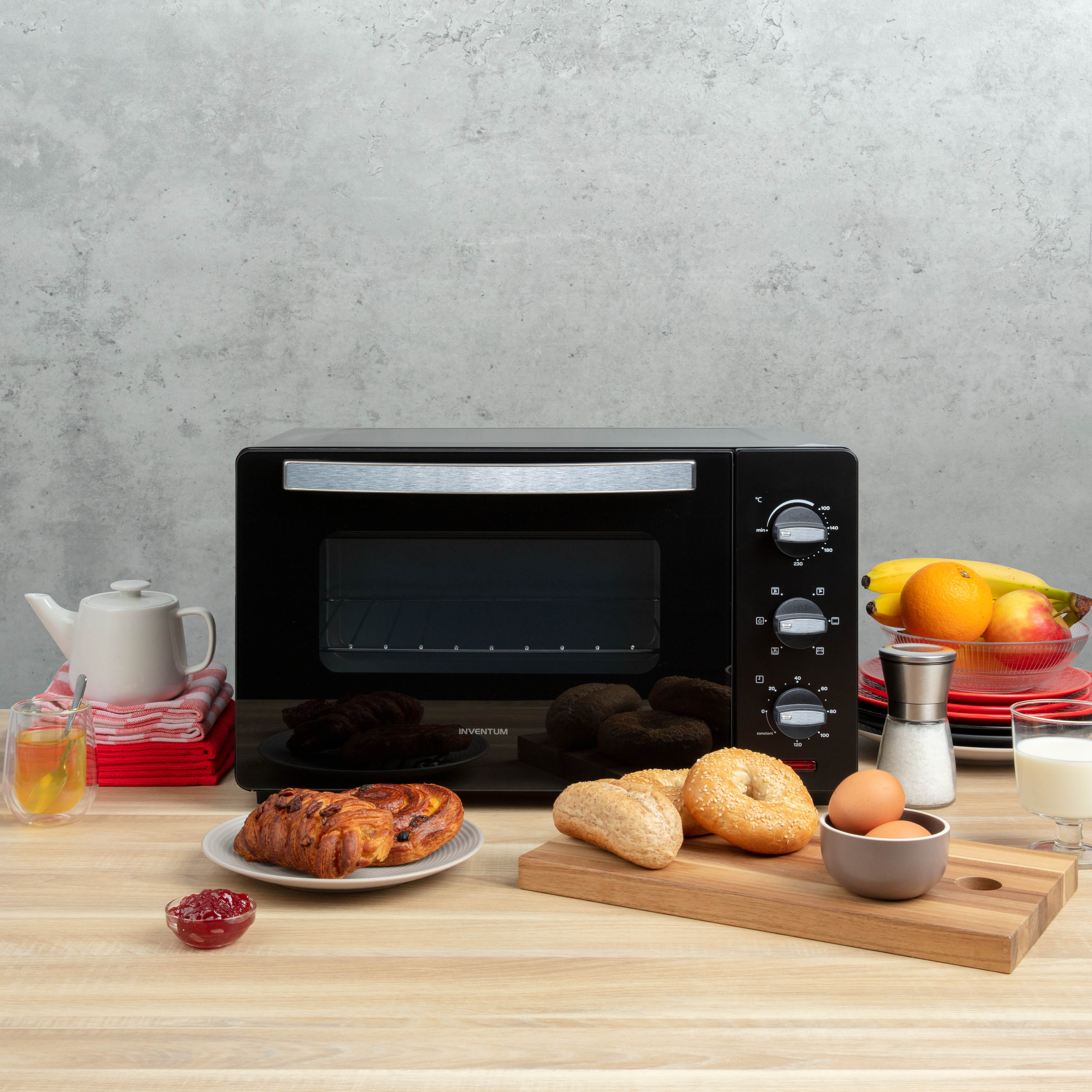 Ein schwarzer Toaster-Ofen mit Essen und einem Teller, mit Obst und anderen Gegenständen auf einem Holztisch.