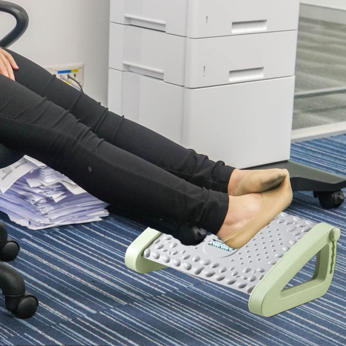Füße einer Person auf einer Fußstütze im Büro. Blauer Teppich, weißer Schreibtisch.