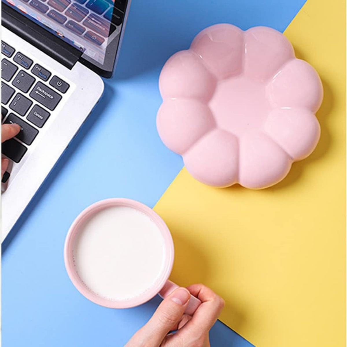 Rosa Tasse mit Milch, rosa blütenförmiger Teller, Laptop. Blauer und gelber Hintergrund.