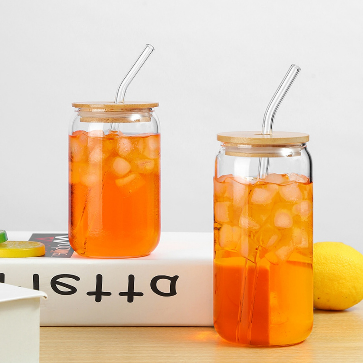 Zwei Gläser mit orangener Flüssigkeit, Eis und Strohhalmen, auf weißem Untergrund. Zitrone.