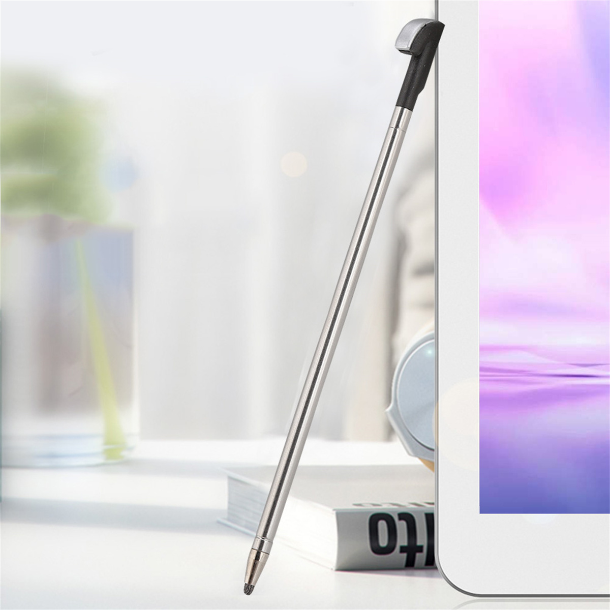 Ein silberner Eingabestift lehnt an einem weißen Tablet. Der Hintergrund ist unscharf mit Fenster und Schreibtisch.