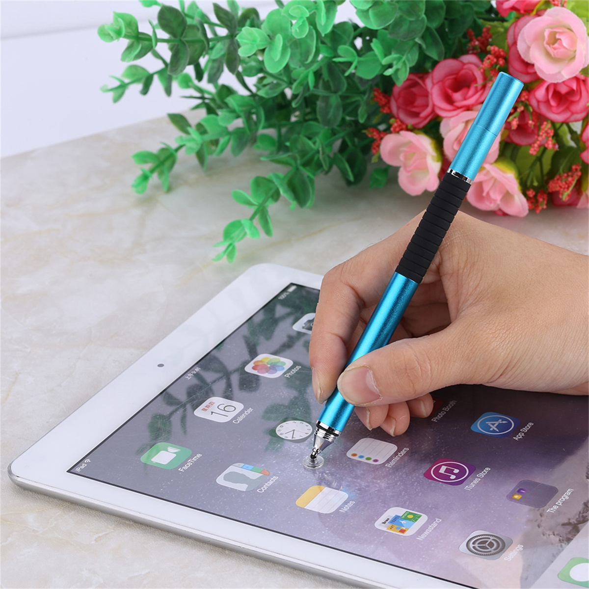 Eine Person benutzt einen blauen Stift auf einem Tablet, in der Nähe eines Blumenarrangements.