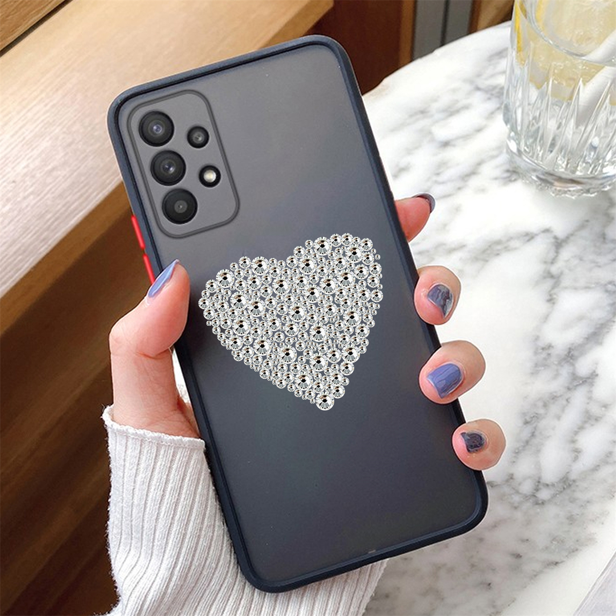 Hand hält ein Telefon mit herzförmiger Dekoration aus silbernen Strasssteinen.