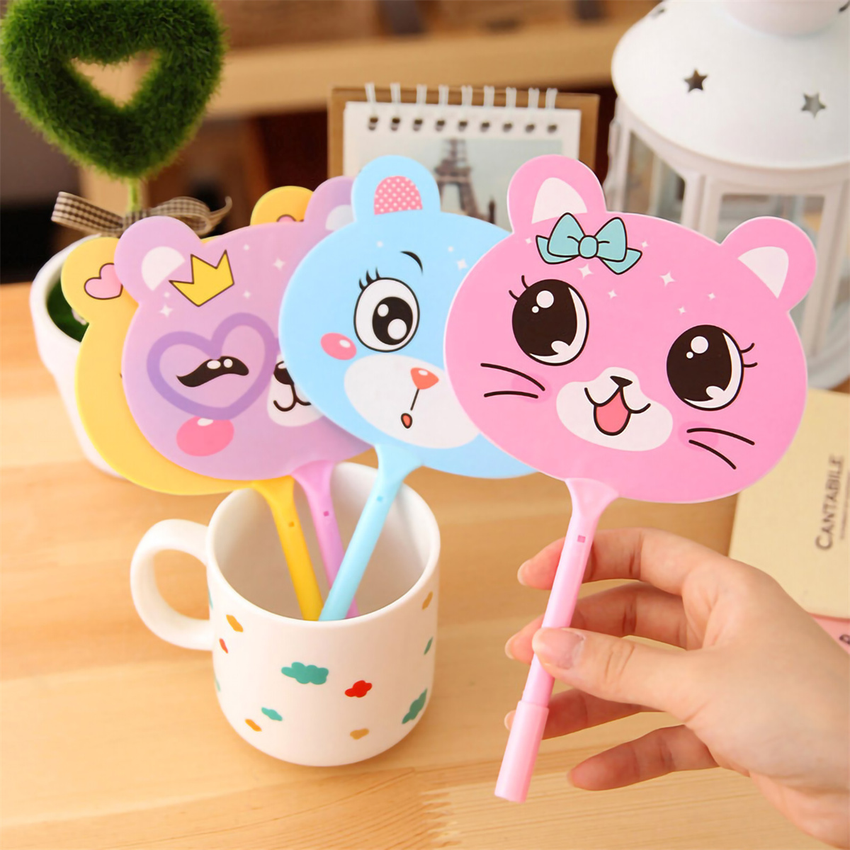 Hand, die einen rosa katzenförmigen Fächer hält, mit anderen Fächern in einer Tasse.