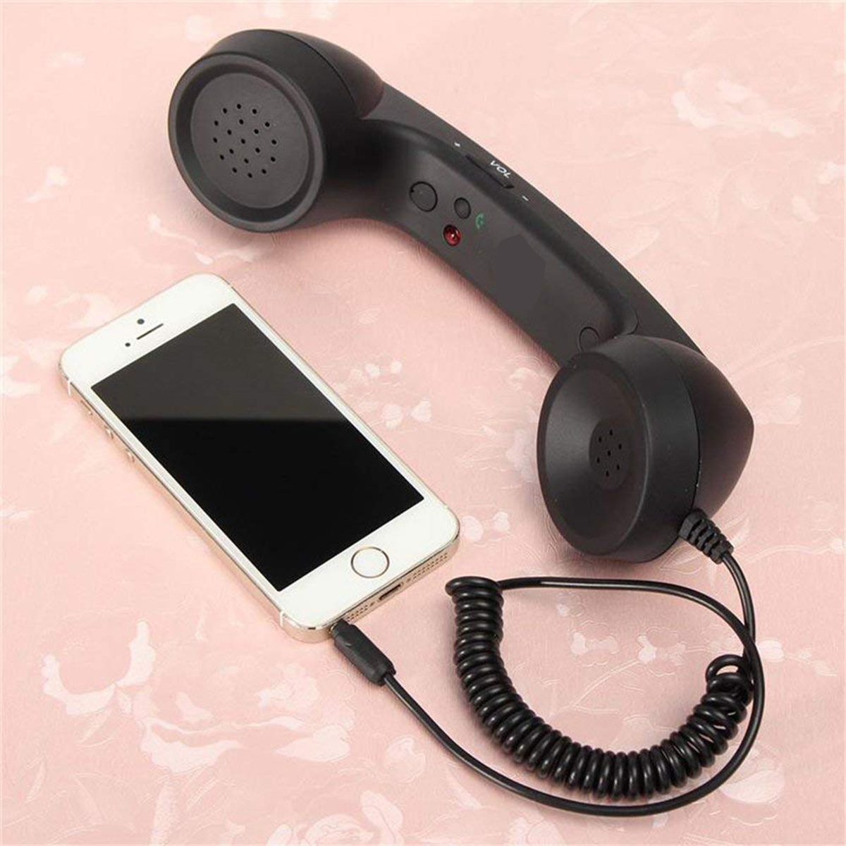 Schwarzer Telefonhörer, verbunden mit einem weißen Telefon mit Kabel auf rosa Oberfläche.