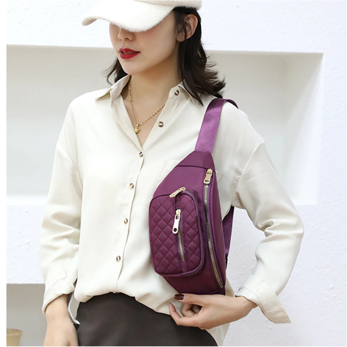 Eine Frau mit einer Handtasche, die einen Hut trägt. Die Handtasche ist dunkelviolett mit goldenen Reißverschlüssen und Steppmuster.