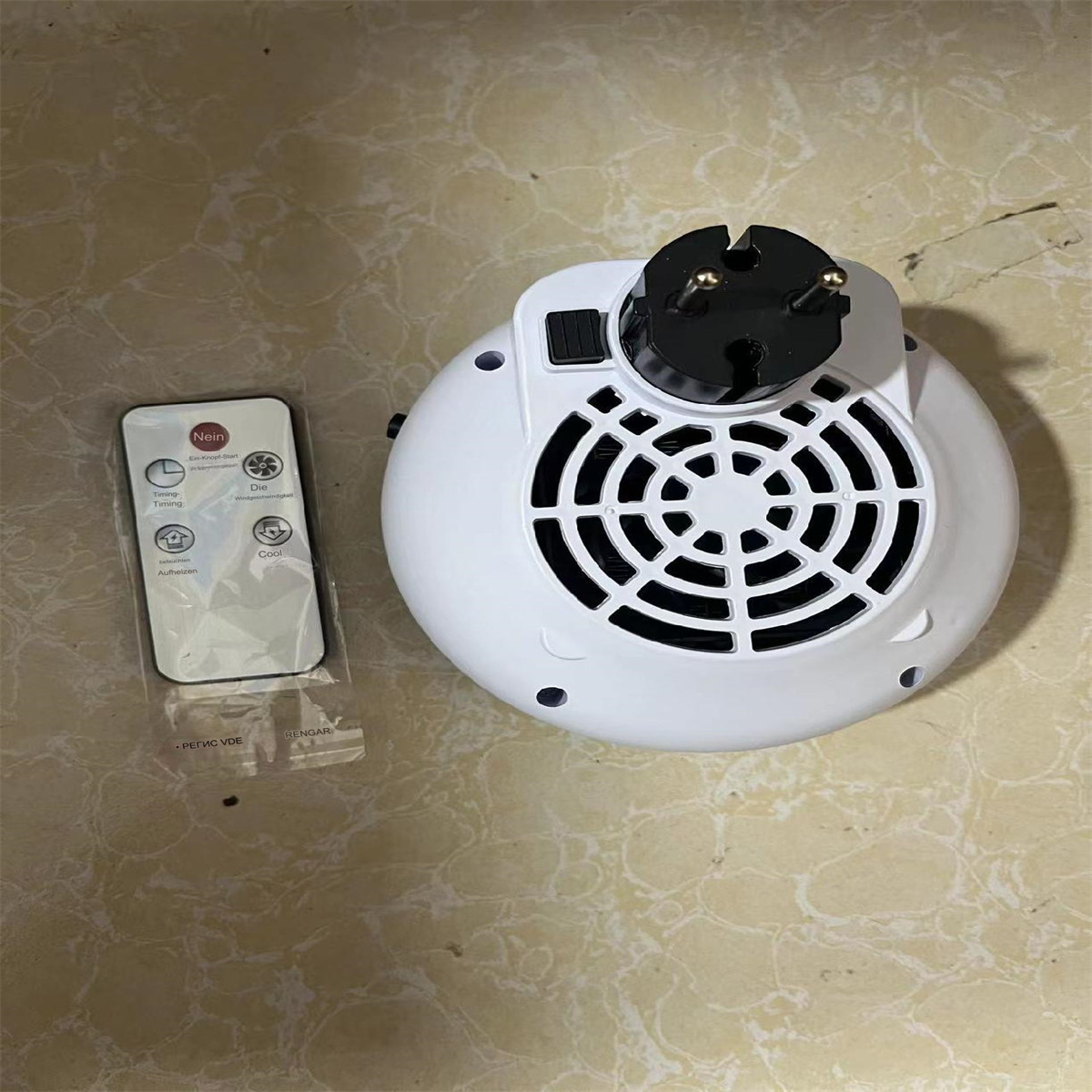 Weißer, runder Mini-Heizlüfter mit Stecker und Fernbedienung mit Tasten.