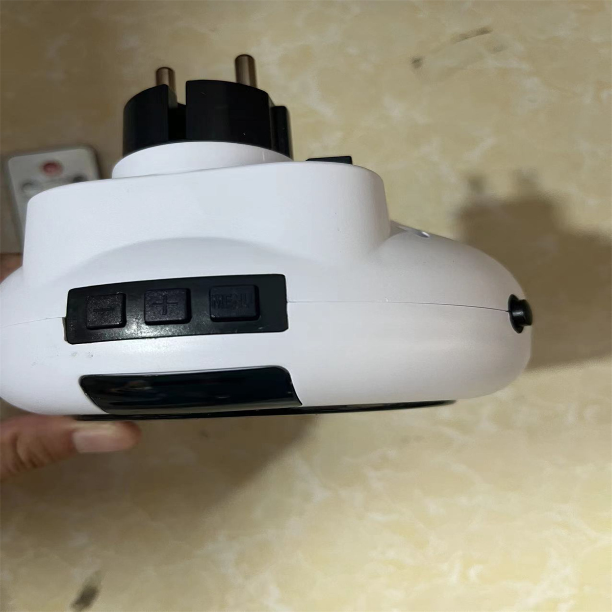 Weißer Netzadapter mit schwarzen Knöpfen und Stecker. Hand hält ihn, auf hellem Hintergrund.