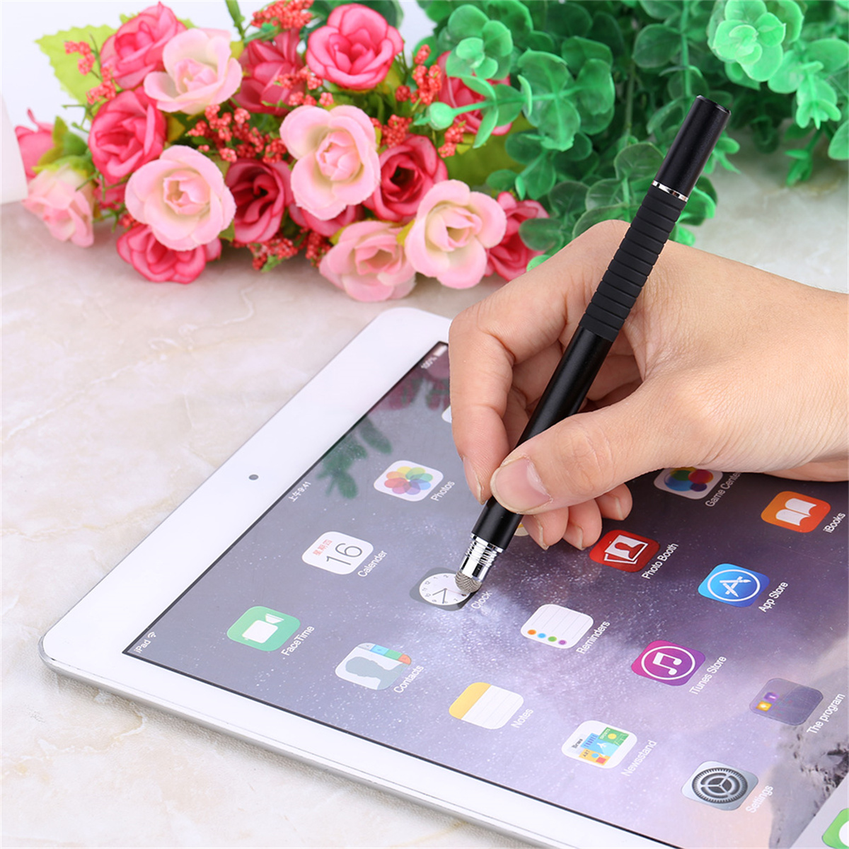 Eine Hand hält einen schwarzen Stift über einem iPad, das Apps anzeigt.