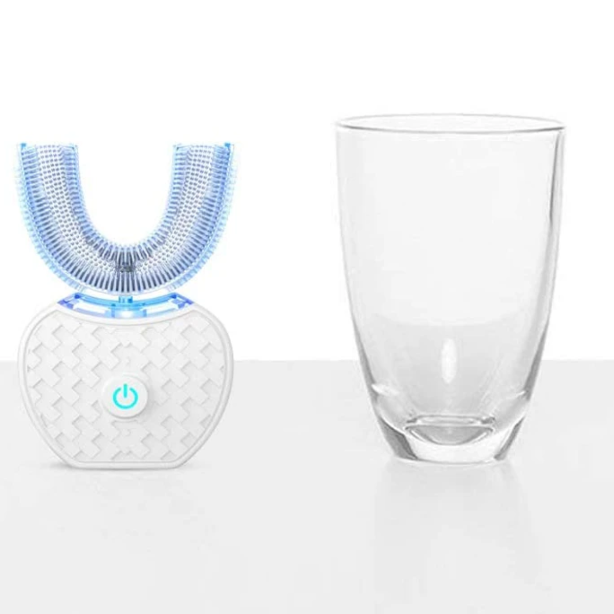 Eine elektrische Zahnbürste und ein Glas. Die Zahnbürste ist weiß und U-förmig. Das Glas ist hoch und klar.
