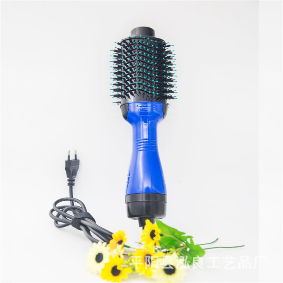 Eine blau-schwarze Haartrocknerbürste mit Borsten. Ein Netzkabel und Blumen darunter.