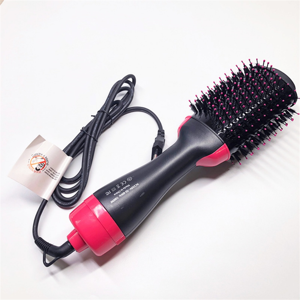 Eine schwarz-rosa Haarbürste auf weißer Oberfläche. Die Bürste hat ein schwarzes Netzkabel.