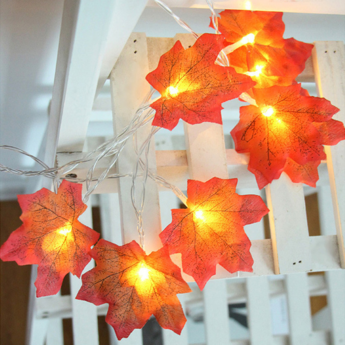 Lichterkette mit orangefarbenen blattförmigen Lichtern auf weißem Holz.