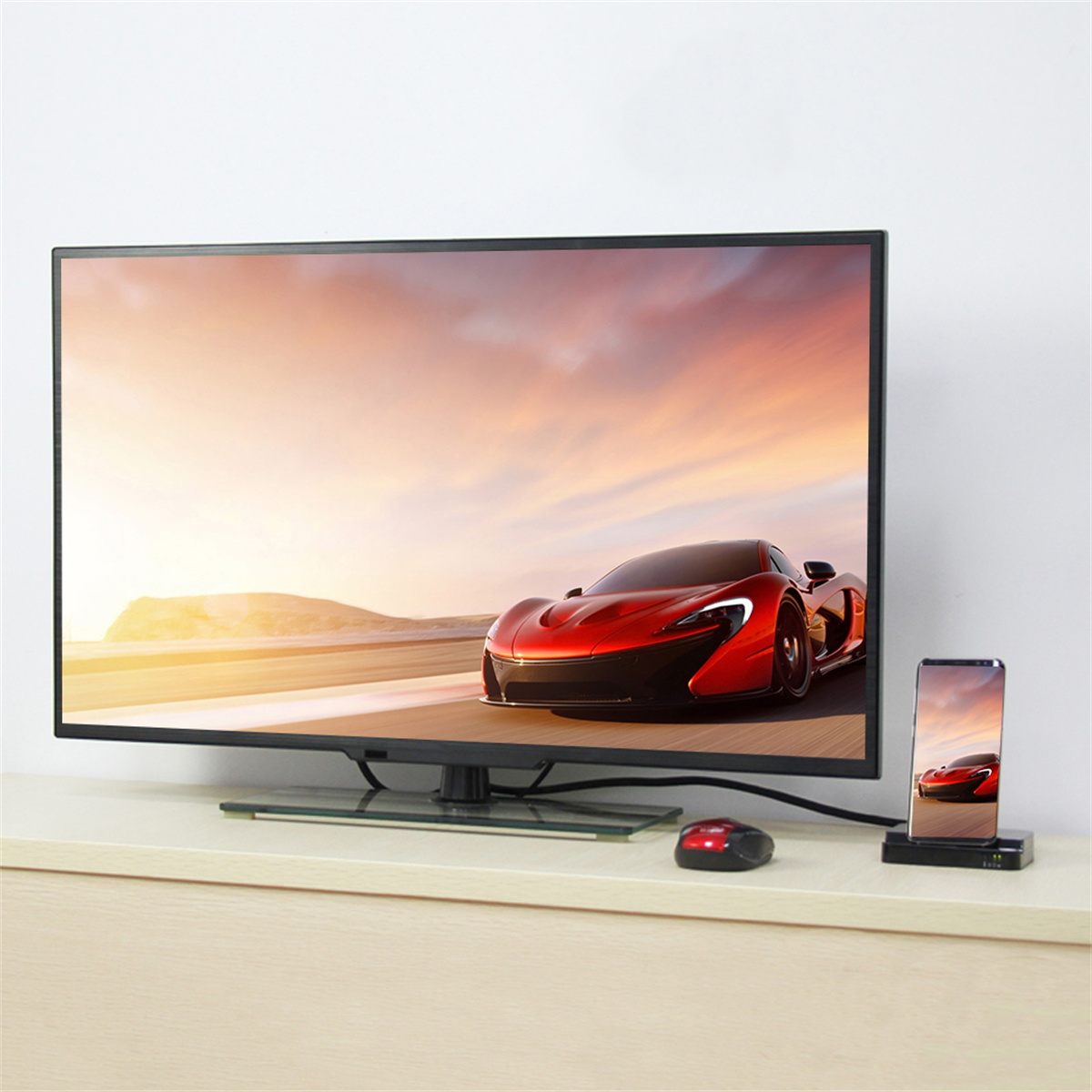 Ein Fernseher mit einem Sportwagen und ein Telefon mit demselben Bild. Beides auf einem weißen Tisch.