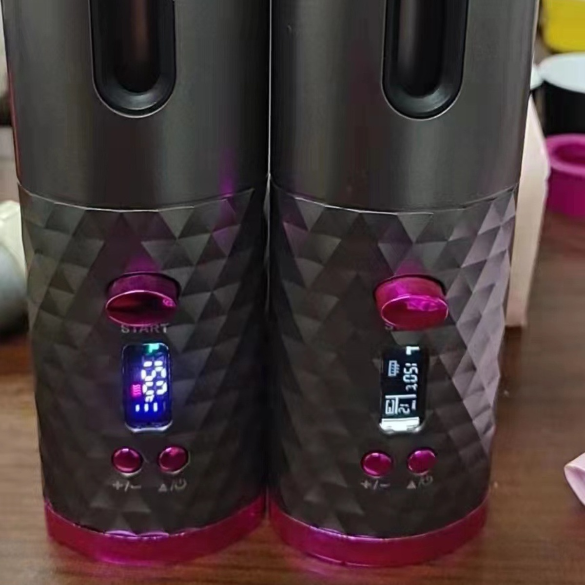 Zwei Lockenstäbe, dunkel mit rosa Knöpfen. Sie haben digitale Bildschirme mit Einstellungen.