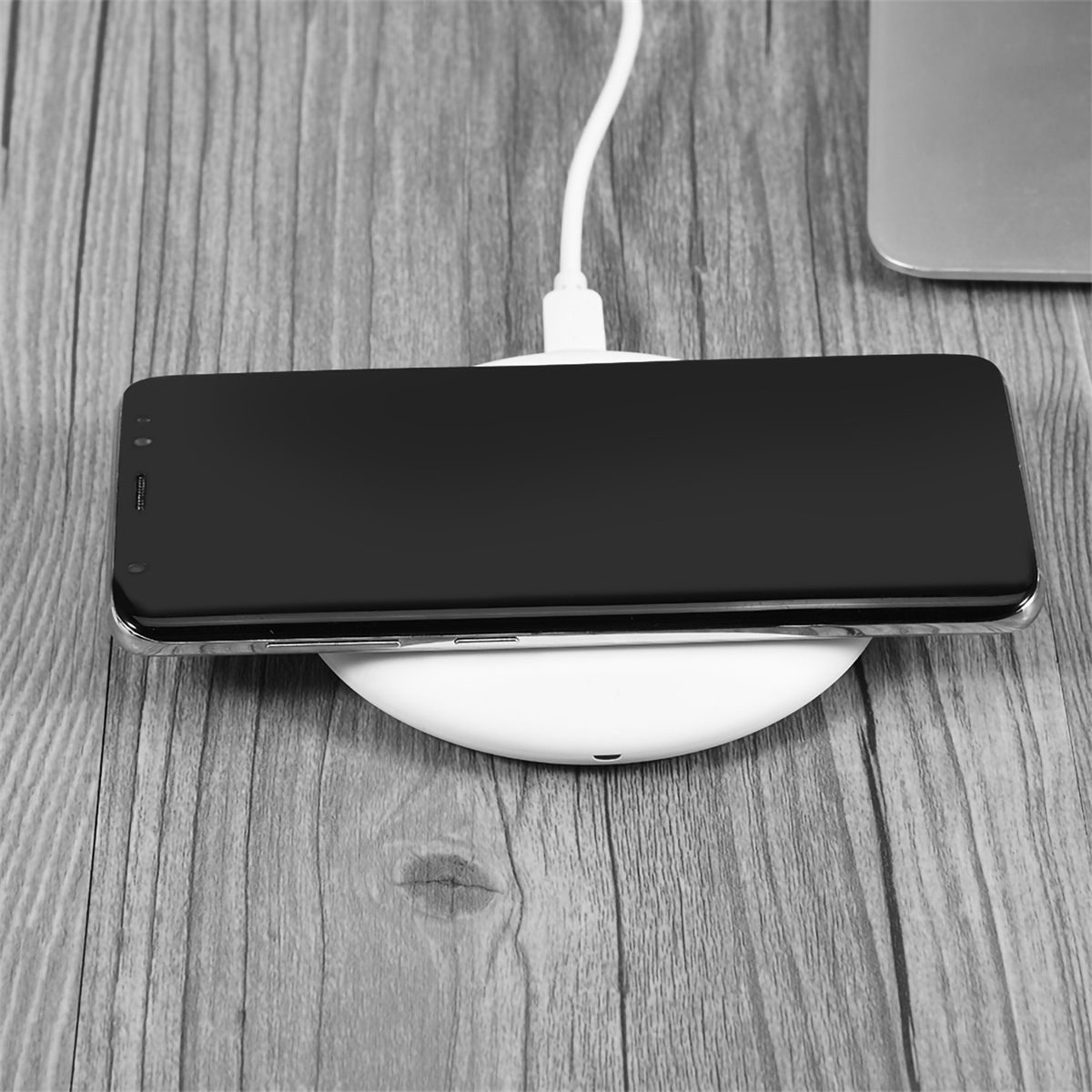 Schwarzes Smartphone auf einem weißen kabellosen Ladepad auf einer Holzoberfläche.