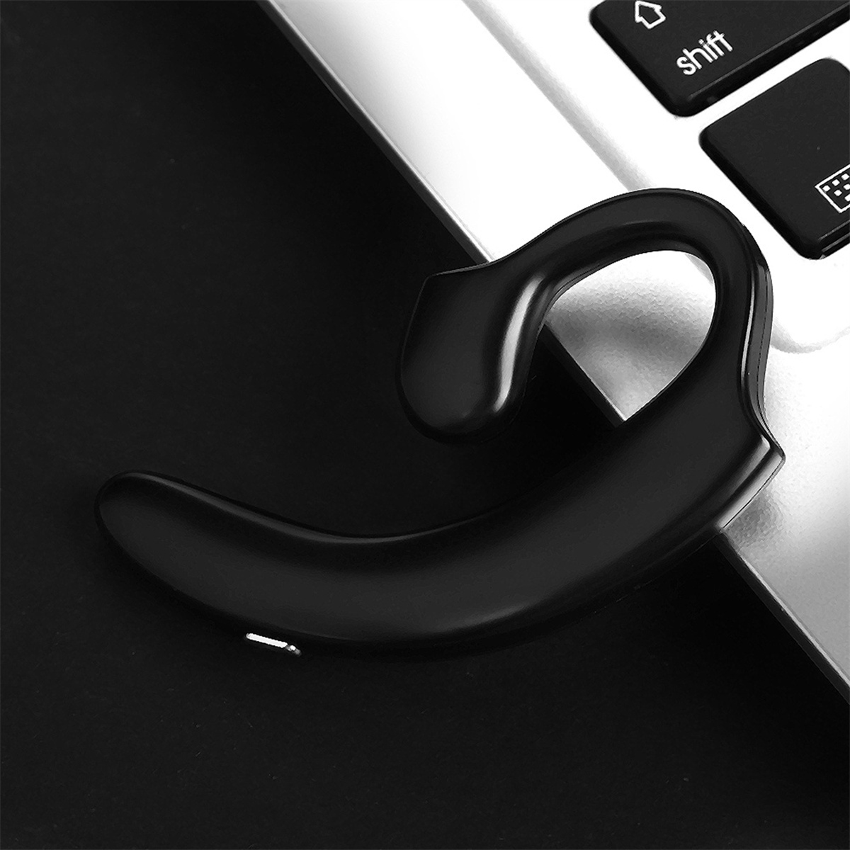 Ein schwarzes Bluetooth-Headset auf einer Laptop-Tastatur, in der Nähe der „Shift“-Taste.