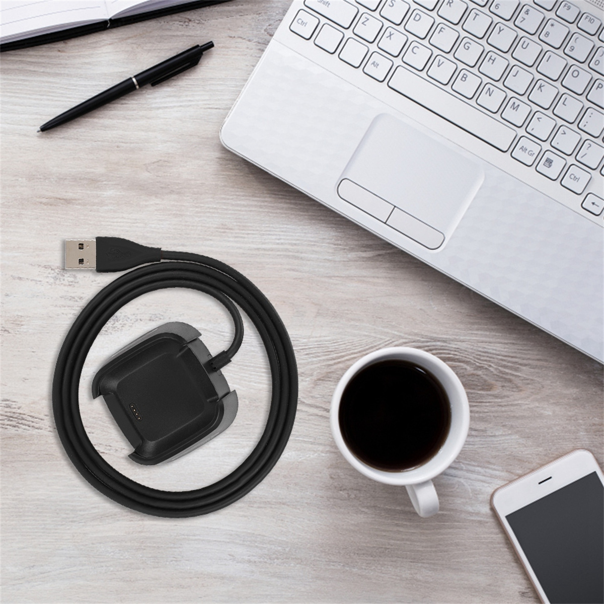 Eine schwarze Ladestation und ein Kabel, eine Tasse Kaffee, ein Telefon und ein Laptop auf einem Holztisch.