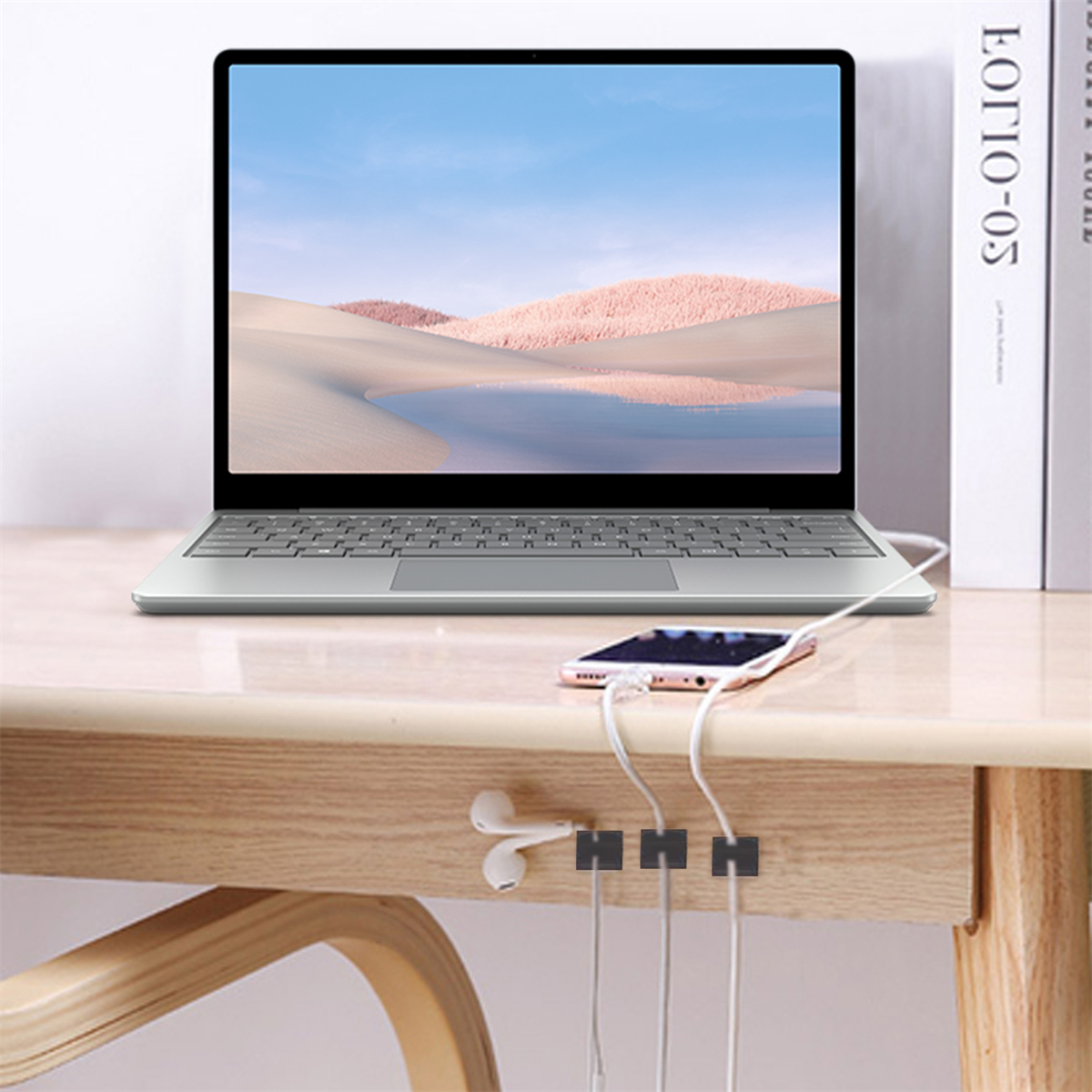 Laptop auf einem Holztisch mit Telefon und Kopfhörerkabeln, gehalten von schwarzen Clips.