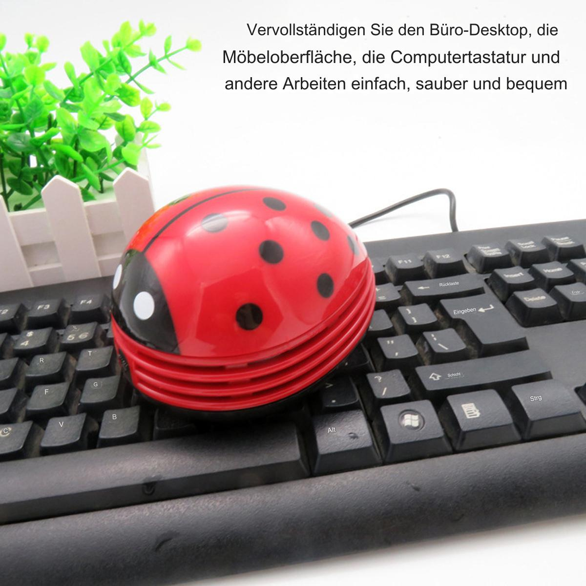 Ein roter Marienkäfer-Staubsauger auf einer schwarzen Tastatur, mit grünen Pflanzen im Hintergrund.