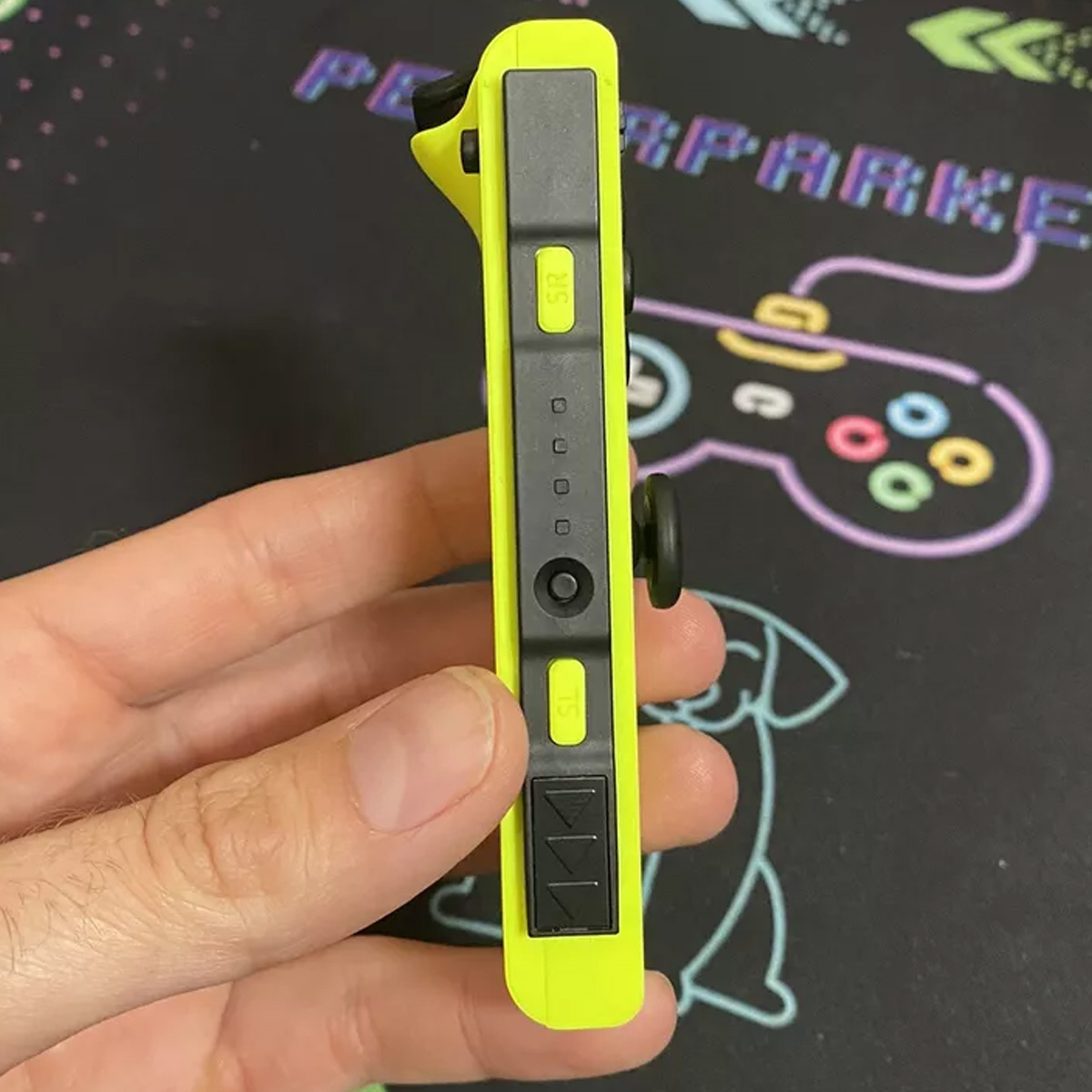 Eine Hand hält einen neongrünen Controller für eine Spielkonsole. Schwarze Tasten sind sichtbar.