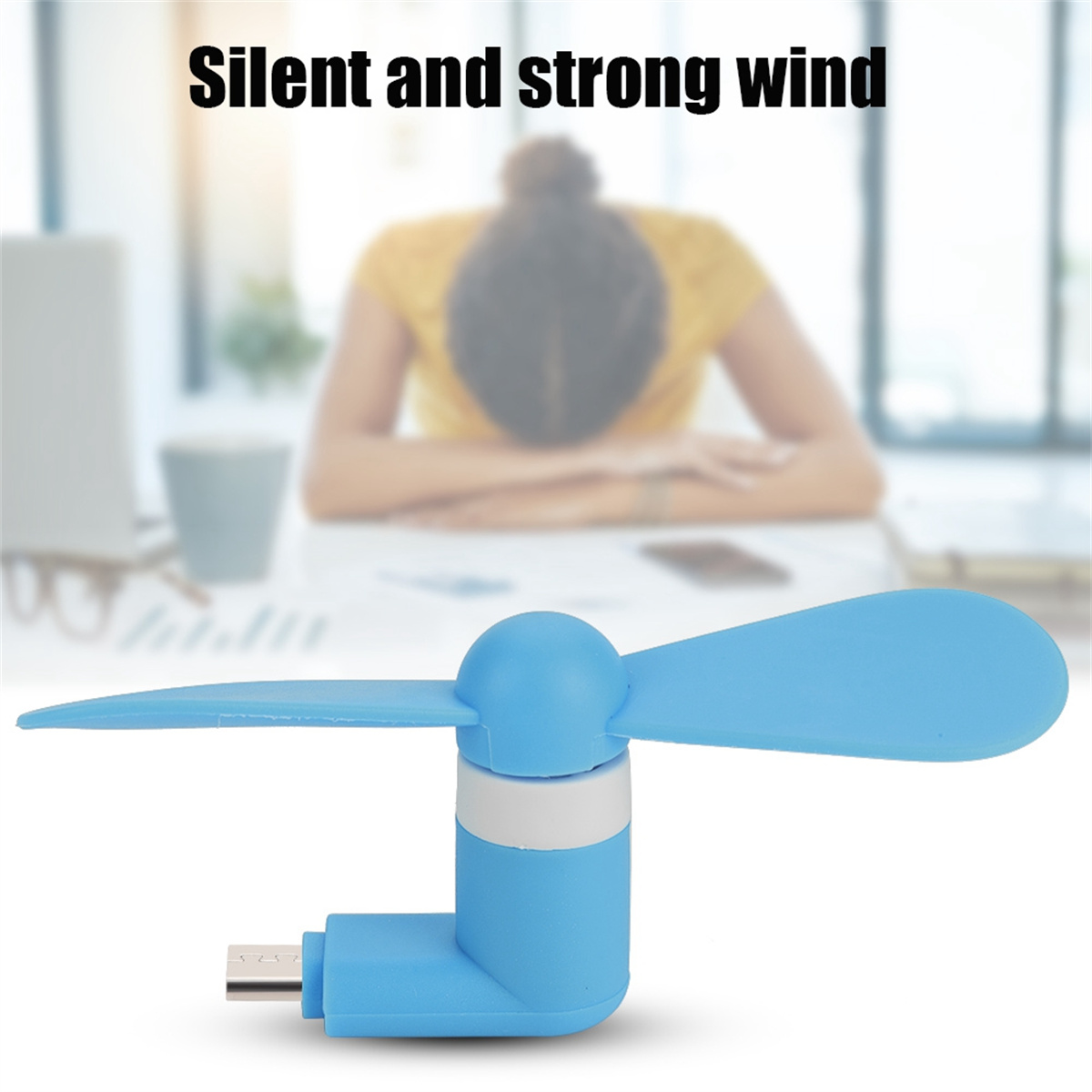 Blauer Mini-Ventilator mit zwei Flügeln. Eine Frau sitzt verschwommen im Hintergrund. Text liest: Silent and strong wind.