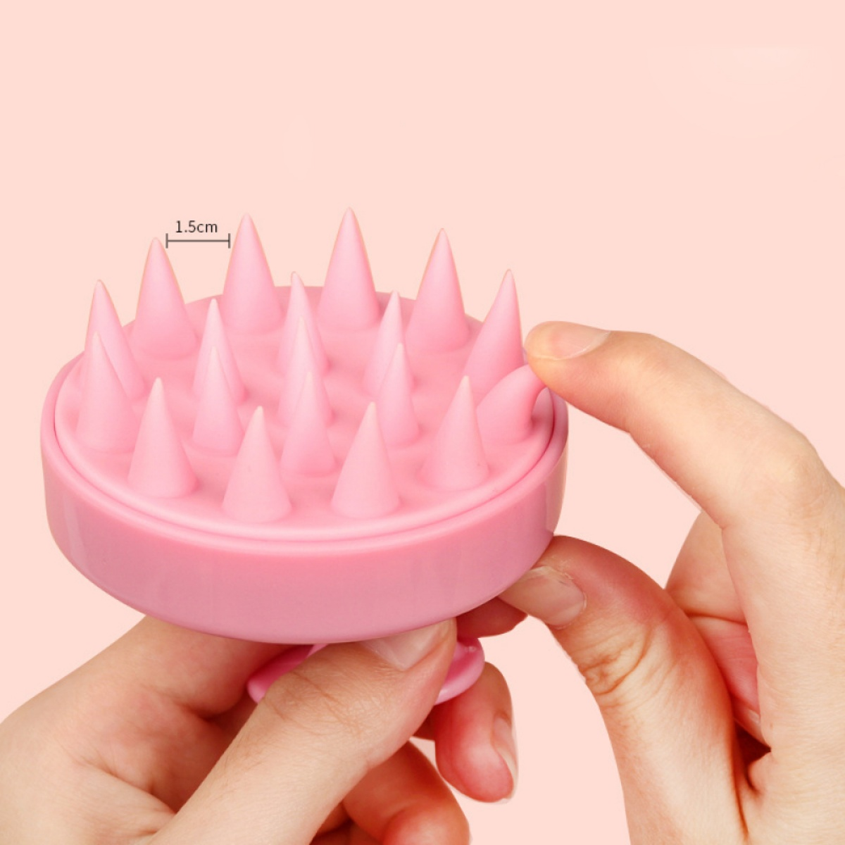 Rosa Kopfhautmassagegerät mit konischen Stacheln, das von zwei Händen vor rosa Hintergrund gehalten wird.