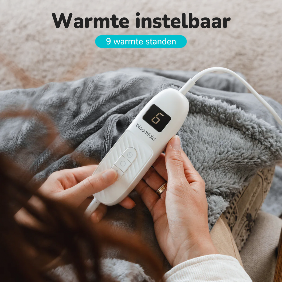 Person's hands holding a white device with a digital display. Grey blanket background.