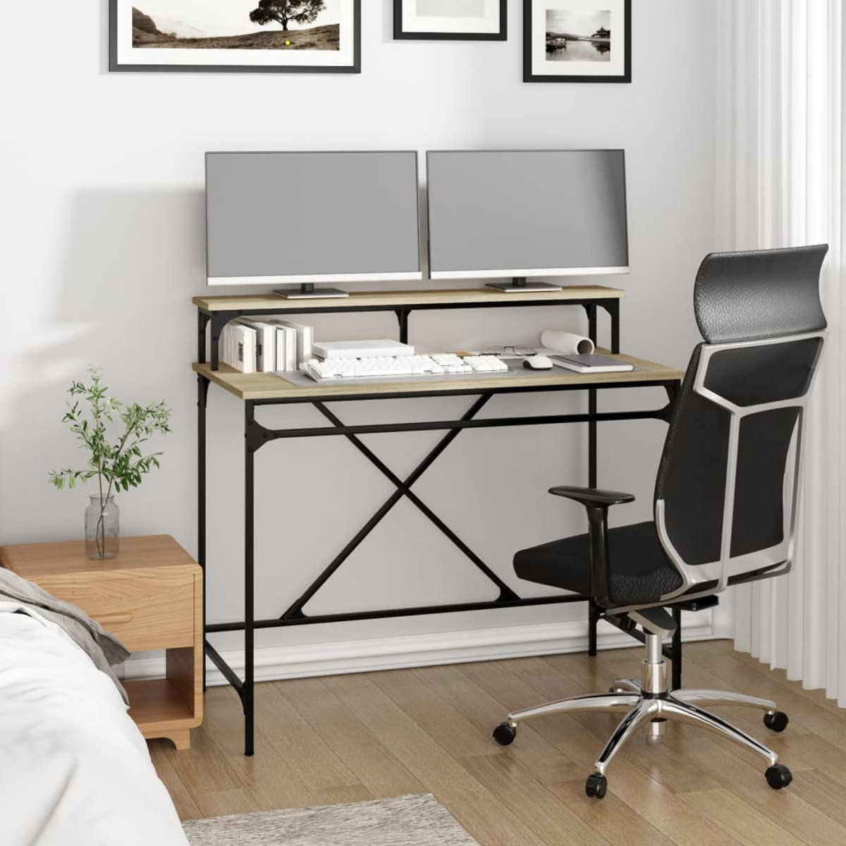 Ein Computertisch mit zwei Monitoren, einer Tastatur und einem schwarzen Stuhl. Das Zimmer hat ein Bett.