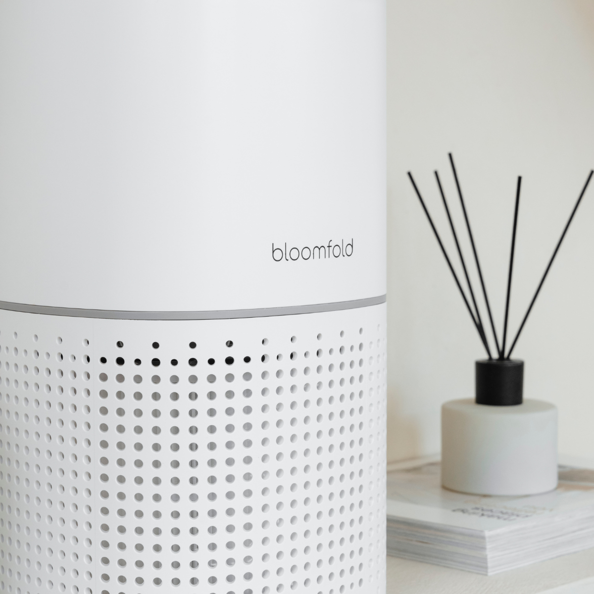 Purificatore d'aria bianco con etichetta 'bloomfold' e diffusore a bastoncini nero su superficie bianca.