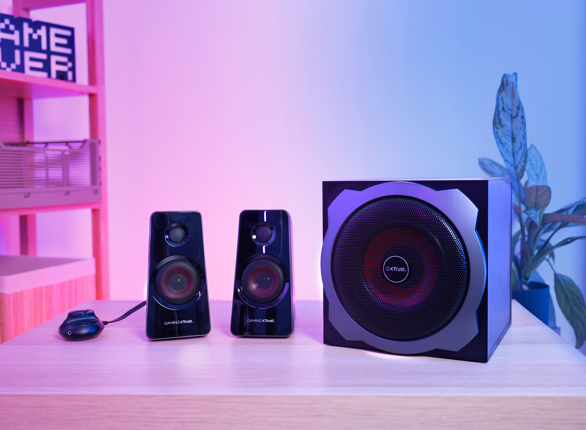 Black speakers and subwoofer on a wooden table. Pink and blue background.