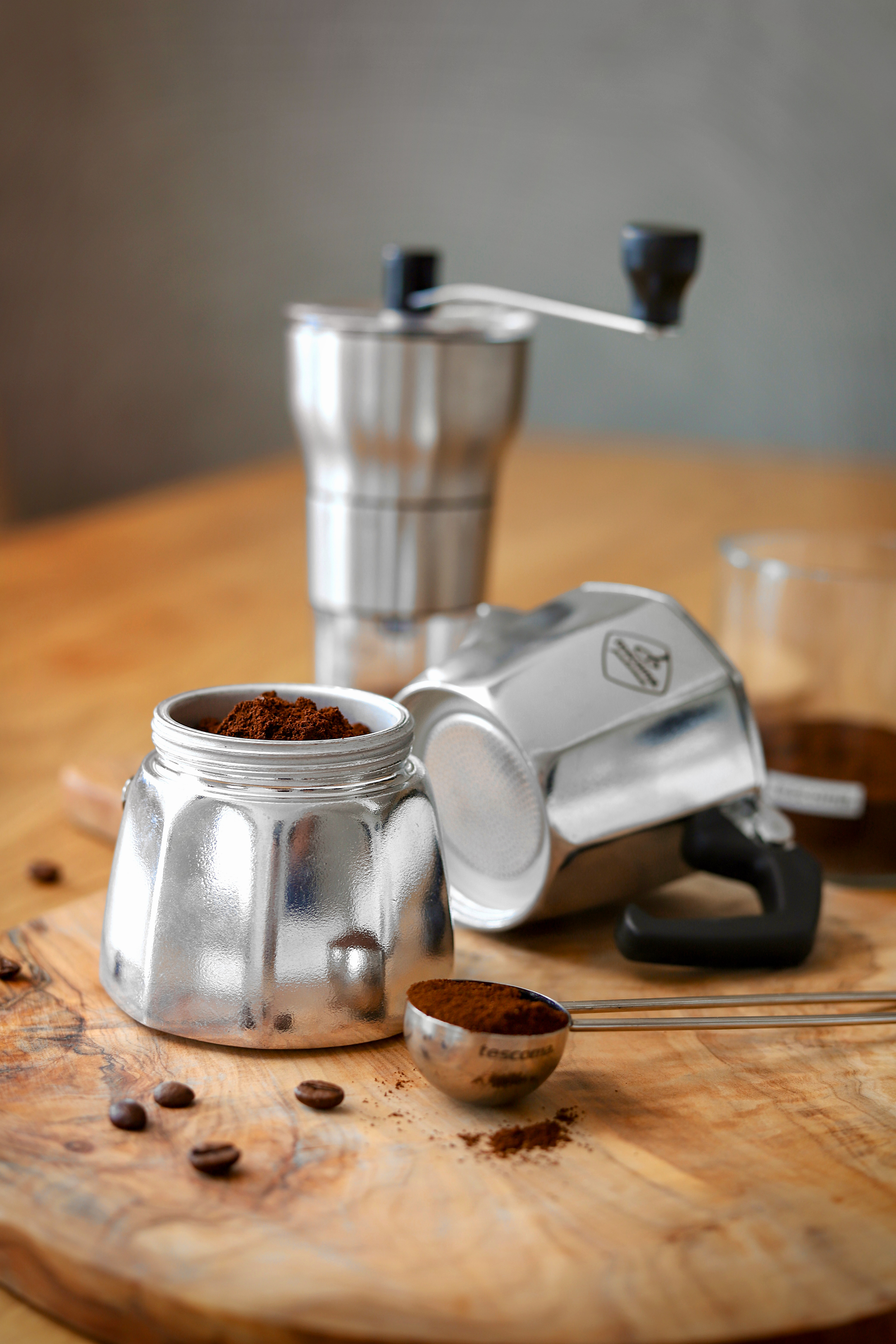 Set macchina caffè: macinacaffè, moka e cucchiaio con caffè macinato su tagliere.
