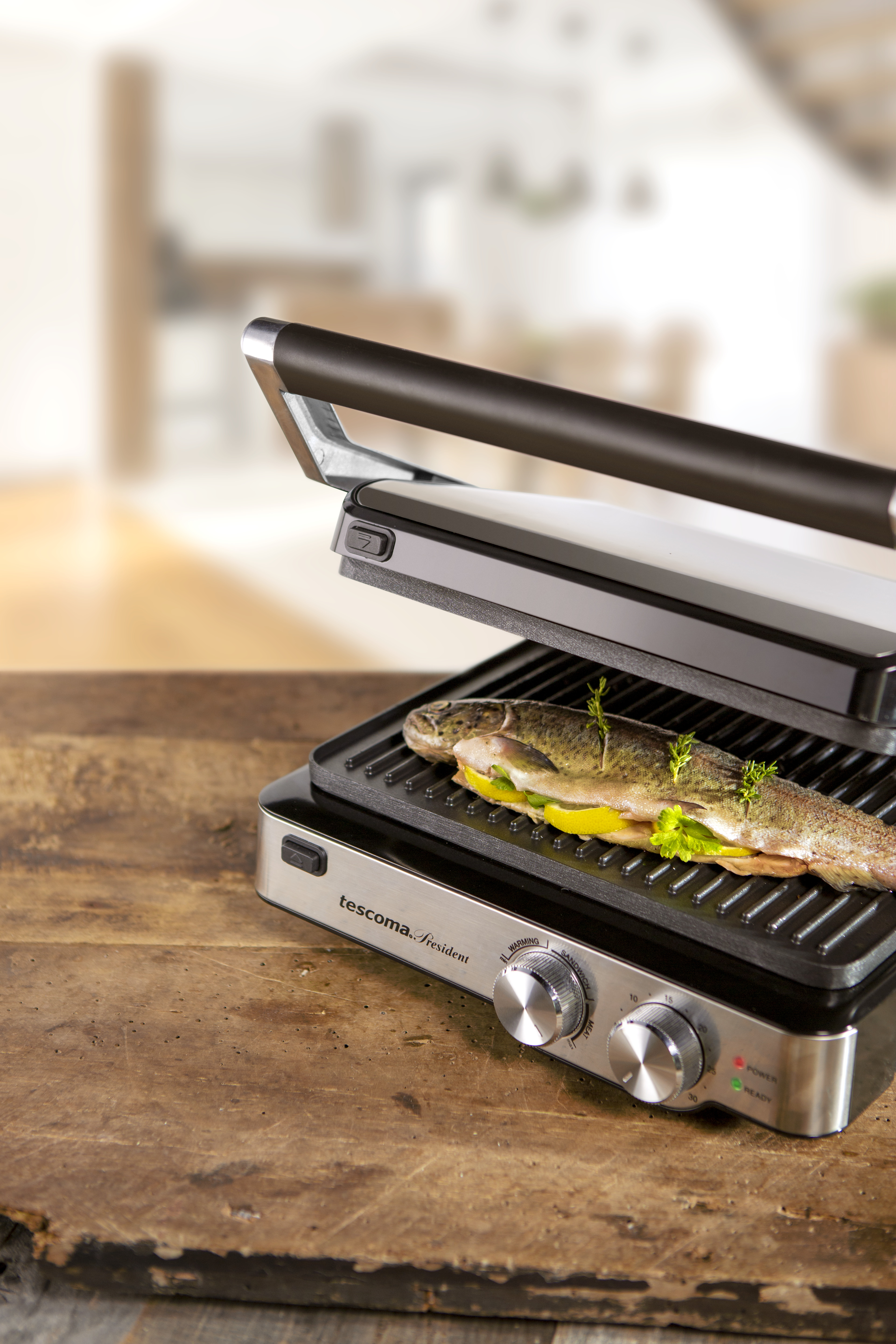 Ein Fisch wird auf einem Tescoma-Grill gegrillt. Der Grill steht auf einer Holzoberfläche.
