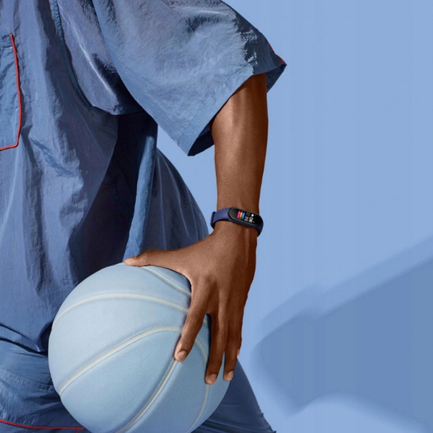 Persona en azul sostiene una pelota de baloncesto, con camisa azul y reloj inteligente. Fondo azul claro.