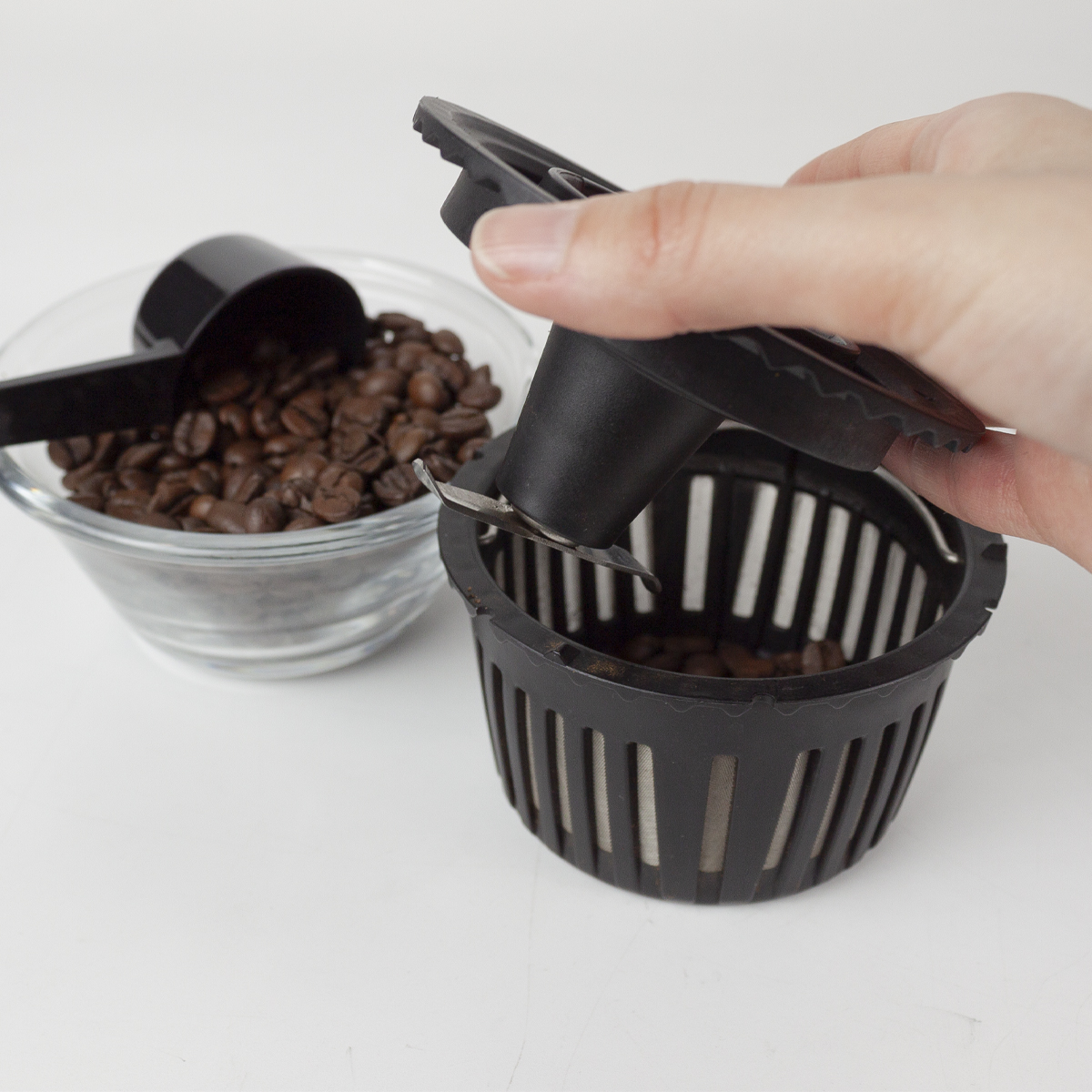 Ręka trzymająca kosz do mielenia nad pojemnikiem z ziarnami kawy.