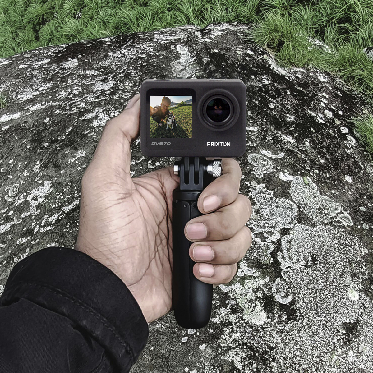 Ręka trzyma kamerę sportową na statywie. Ekran kamery pokazuje osobę i psa.