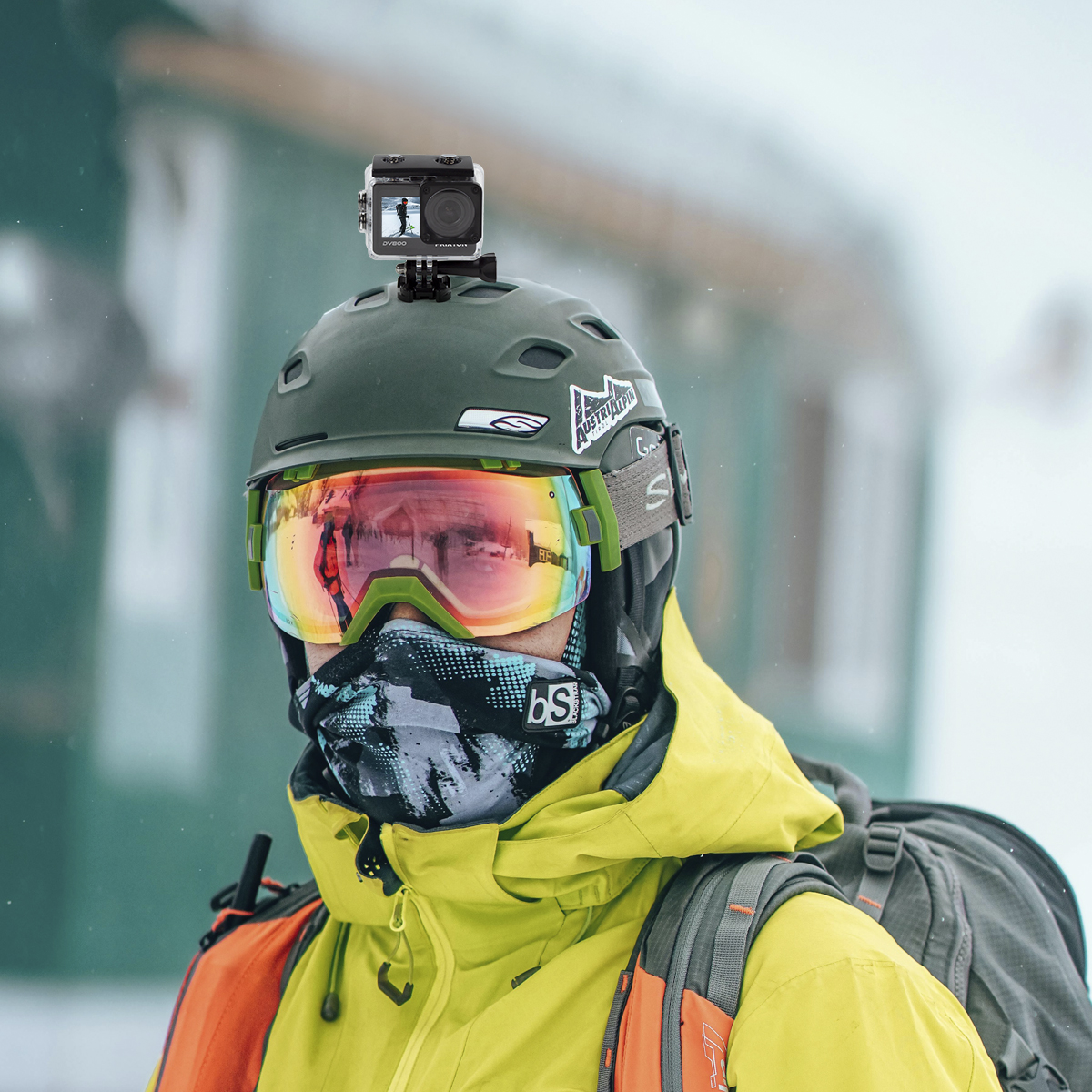 Narciarz w kasku, goglach i kamerą. Narciarz ma na sobie żółtą kurtkę. Śnieg w tle.