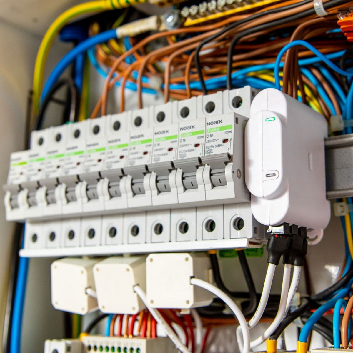 Panel eléctrico con disyuntores y cables. Dispositivo inteligente blanco adjunto. Cables de varios colores.