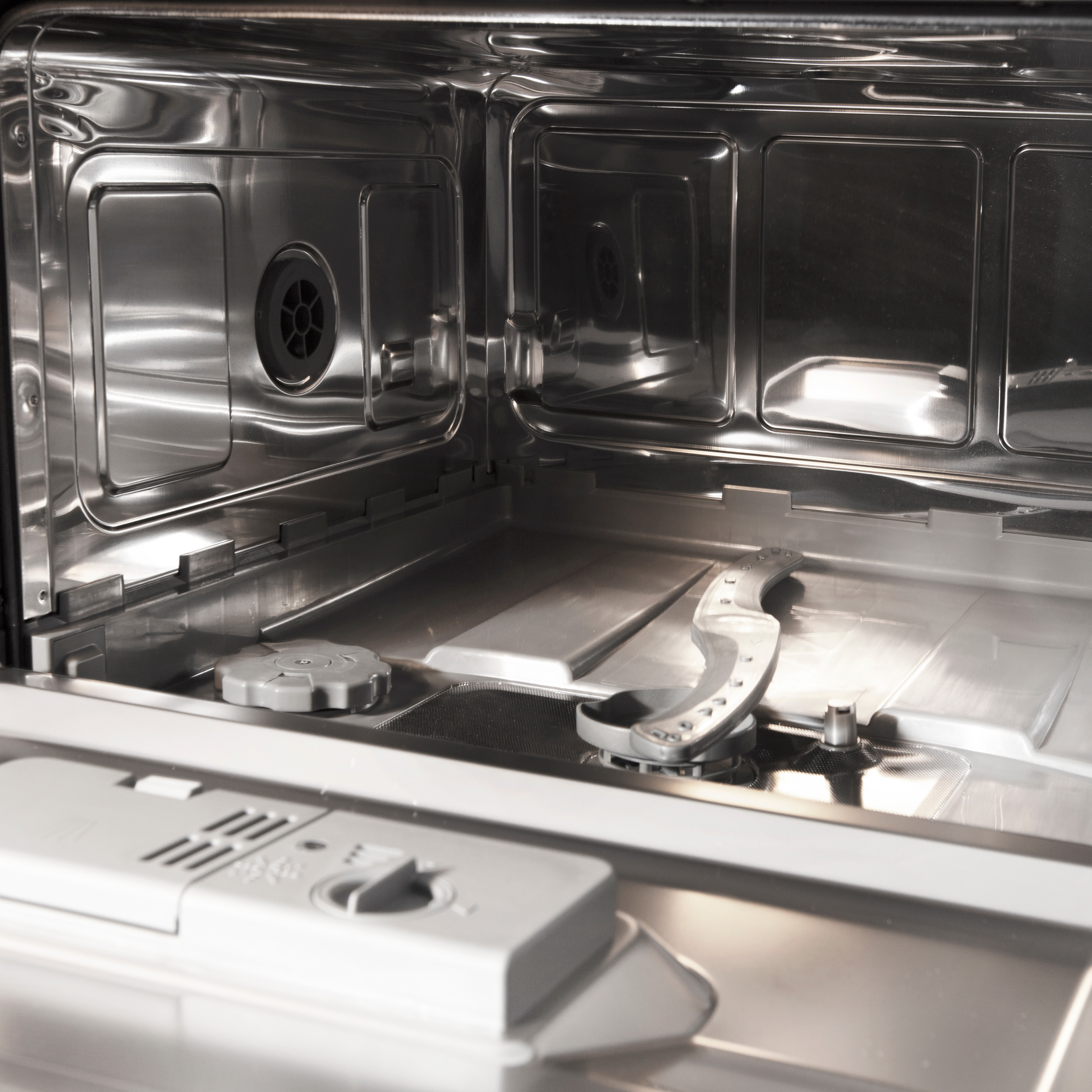 Interior of a dishwasher. Stainless steel surfaces with a spray arm and a gray compartment.